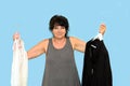 aged woman with a confused look and a smile holds hangers with clothes, choice content on a blue background