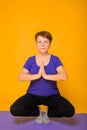 Aged woman doing yoga on a purple rug. Studio photo on a yellow background Royalty Free Stock Photo