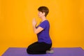 Aged woman doing yoga on a purple rug. Studio photo on a yellow background Royalty Free Stock Photo