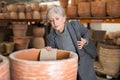 Aged woman selecting decorative earthenware pot in shop