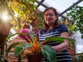 An aged woman is watering home plants from a pink watering can