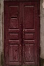 Aged wooden door painted maroon. Vintage house facade with a door. Wood vinous texture of a door. Old burgundy grunge texture Royalty Free Stock Photo