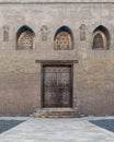 Wooden weathered door, and windows with perforated stucco floral patterns on stone bricks wall