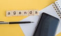 Agenda plan written on wooden cubes on desktop with pen  phone and paper Notepad on yellow background  top view  flat layout Royalty Free Stock Photo