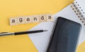 Agenda plan written on wooden cubes on desktop with pen  phone and paper Notepad on yellow background  top view  flat layout Royalty Free Stock Photo