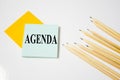 Agenda word written on a yellow piece of paper and white background with pencils lying next to it Royalty Free Stock Photo