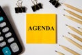 Agenda word written on a yellow piece of paper and white background with pencils lying next to it Royalty Free Stock Photo