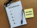 Agendas text on a note pad with pen, sticky note and glasses background.