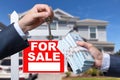 Agent Handing Over Keys as Buyer is Handing Over Cash for House with Home and For Sale Real Estate Sign Behind. Royalty Free Stock Photo