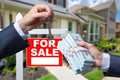 Agent Handing Over Keys as Buyer is Handing Over Cash for House with Home and For Sale Real Estate Sign Behind. Royalty Free Stock Photo