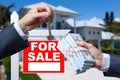 Agent Handing Over Keys as Buyer is Handing Over Cash for House with Home and For Sale Real Estate Sign Behind. Royalty Free Stock Photo