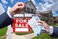 Agent Handing Over Keys as Buyer is Handing Over Cash for House with Home and For Sale Real Estate Sign Behind. Royalty Free Stock Photo