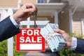 Agent Handing Over Keys as Buyer is Handing Over Cash for House with Home and For Sale Real Estate Sign Behind. Royalty Free Stock Photo