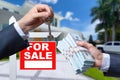 Agent Handing Over Keys as Buyer is Handing Over Cash for House with Home and For Sale Real Estate Sign Behind. Royalty Free Stock Photo