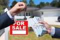 Agent Handing Over Keys as Buyer is Handing Over Cash for House with Home and For Sale Real Estate Sign Behind. Royalty Free Stock Photo