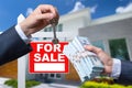 Agent Handing Over Keys as Buyer is Handing Over Cash for House with Home and For Sale Real Estate Sign Behind. Royalty Free Stock Photo