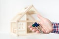 Agent`s hand hold keys against house model on background. Realtor sale offer. Real estate investment proposition. Buying new ho