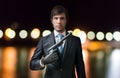 Agent or spy holds pistol in hand at night. Blurred lights in background