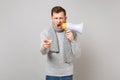 Aggression young man in gray sweater, scarf scream in megaphone, pointing index finger on camera isolated on grey Royalty Free Stock Photo
