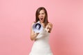 Aggressive angry bride woman in wedding dress screaming in megaphone, pointing index finger on camera on pink