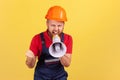 Aggressive bearded worker wearing protective helmet and blue overall holding megaphone and screaming Royalty Free Stock Photo