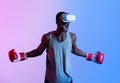 Aggressive black sportsman in VR headset and boxing gloves shouting during his workout in neon light