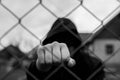 Aggressive teenage boy showing hes fist behind wired fence at the correctional institute, focus on the boys hand