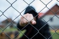 Aggressive teenage boy showing hes fist behind wired fence at the correctional institute, focus on the wired fence