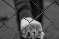 Aggressive teenage boy showing hes fist behind wired fence at the correctional institute, the word hate is written on hes hand