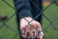 Aggressive teenage boy showing hes fist behind wired fence at the correctional institute, the word hate is written on hes hand