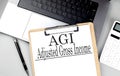 AGI -ADJUSTED GROSS INCOME word on clipboard on laptop with calculator and pen