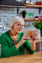 Aging lady lovingly looking at picture sitting at kitchen table