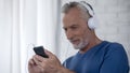 Aging male in headphones scrolling screen of smartphone, using music application