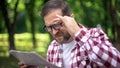 Aging man in eyeglasses trying to read newspaper in park, farsightedness, myopia Royalty Free Stock Photo