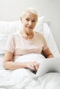 Aging person clicking on laptop in bed of medical center