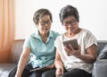 Aging society concept with Asian elderly senior adult women twin sisters using mobile tablet application technology for social