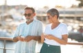 Aging spouses engaging with phones near marina yachts outside
