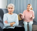 Agitated adult daughter reprimanding upset senior woman on sofa
