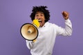 Agitated black teenager shouting into megaphone over violet studio background Royalty Free Stock Photo