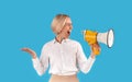 Agitated female public speaker shouting into megaphone on blue studio background Royalty Free Stock Photo