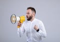 Agitated young man screaming into megaphone on grey studio background