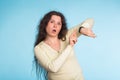 Agitated young woman pointing her wrist watch over blue background Royalty Free Stock Photo