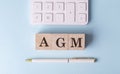 AGM word on wooden block with pen and calculator on blue background Royalty Free Stock Photo