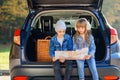 Agreeable boy and girl are looking at the road map while sitting in the auto`s trunk and discussing the move direction Royalty Free Stock Photo