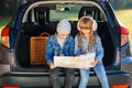 Agreeable boy and girl are looking at the road map while sitting in the auto`s trunk and discussing the move direction