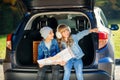 Agreeable boy and girl looking at the road map while sitting in the auto`s trunk and discussing the move direction.