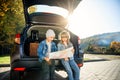 Agreeable boy and girl are looking at the road map while sitting in the auto`s trunk and discussing the move direction Royalty Free Stock Photo