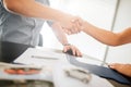 Agreement between two young men. They shake each other`s hands. There are pen, journal and other documents on table Royalty Free Stock Photo