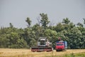 An agricultural combine harvester unloads wheat in a truck in a summer field