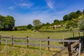 Agricultural parcels with wooden fences dividing land, horse, hiking path and mountain with leafy trees in background